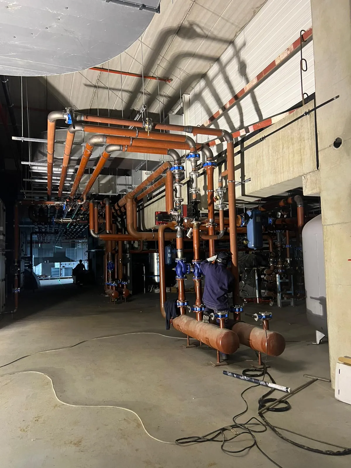 Industriële HVAC-leidinginstallatie met koperen buizen, kleppen en een monteur aan het werk
